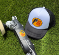 A black and silver RUPC angle grinder with a sanding disc attachment, placed on green artificial turf next to a black and white trucker hat featuring a yellow 'We Don't Fish' logo.